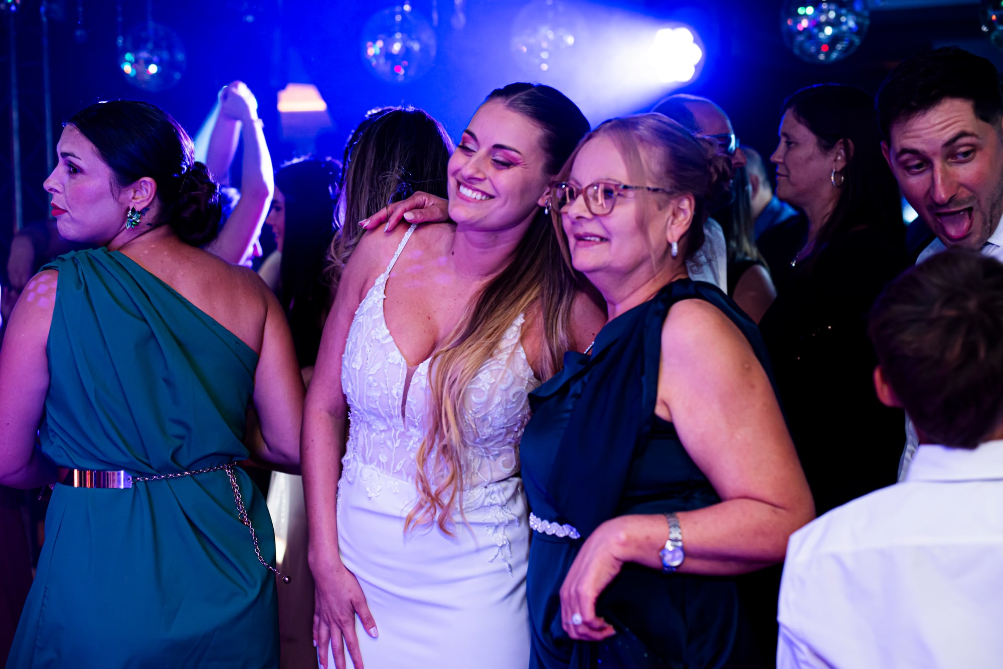 La novia abrazada a su madre en la pista, bajo la luz azul de la fiesta
